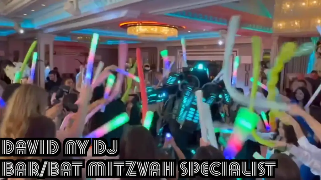 A crowded dance floor with people dancing and waving their hands in a lively party atmosphere. Colorful lights and decorations can be seen in the venue.